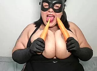 BBW Mary Jhuana eats carrot with another mouth, pierced nipples and tattoos on display.