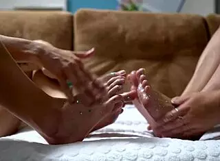 two cuties with shiny legs are playing with a huge rubber cock, giving it a footjob