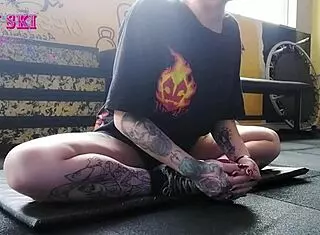 Alternative girl stretches at the gym, showing off her tattoos. 😏